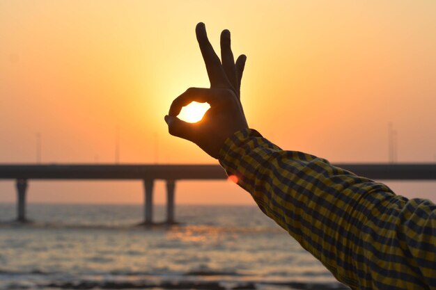 Close-up of silhouette hand against sea during sunset