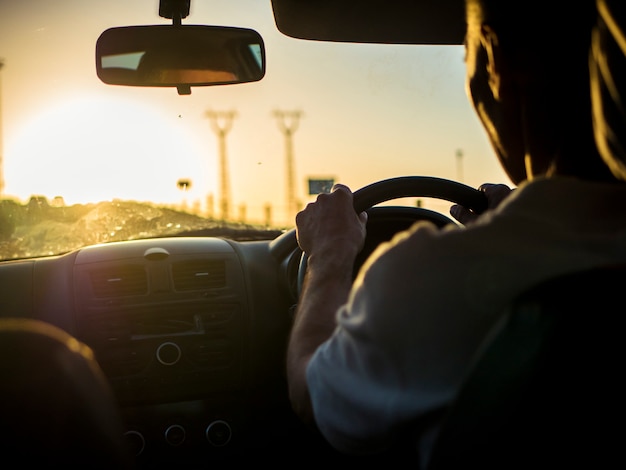 Foto chiuda sulla siluetta dell'uomo che conduce un'automobile su un tramonto durante l'ora dorata