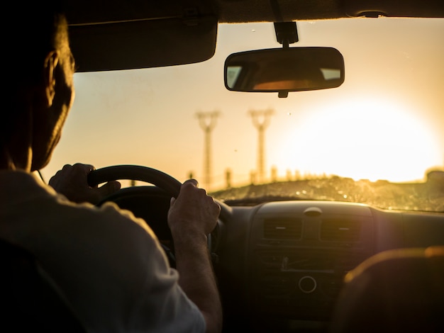 Chiuda sulla siluetta dell'uomo che conduce un'automobile su un tramonto durante l'ora dorata