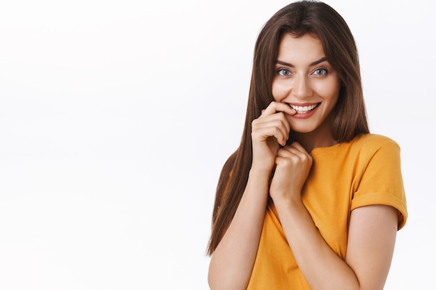 Close-up silly good-looking seductive and sensual feminine brunette woman with long healthy soft hair, touching lip and smiling joyful, standing in lovely cute pose, white background