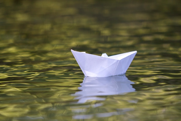 Close-up of simple small white origami paper boat floating quietly in yellow clear river 