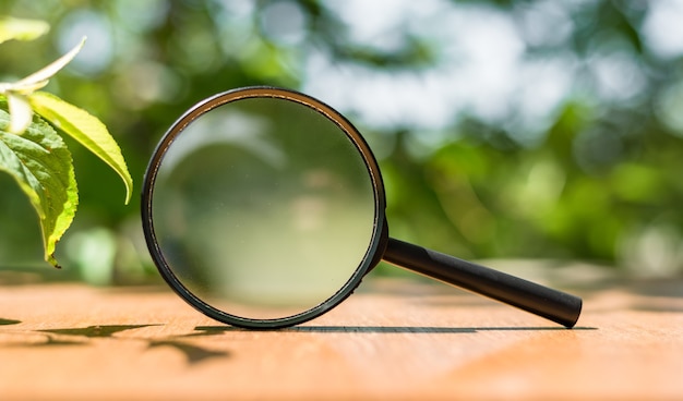 Photo close up single magnifying glass with black handle, leaning on the wooden table on outdoors.