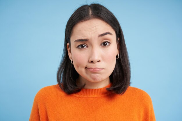 Photo close up of skeptical japanese girl shrugs shoulders and looks confused puzzled stands over blue stu