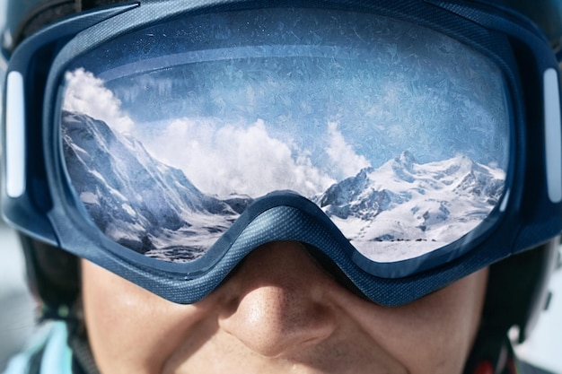 Закройте лыжные очки человека с отражением заснеженных гор.