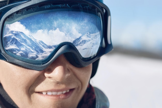 Close up of the ski goggles of a man with the reflection of snowed mountains