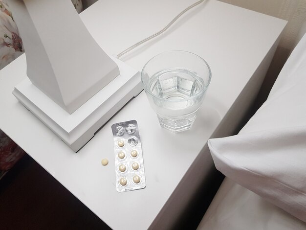 Close-up of sleeping pills and a glass of water prepared for a calm and sound sleep on the bedside table in the bedroom, the concept of health and illness.