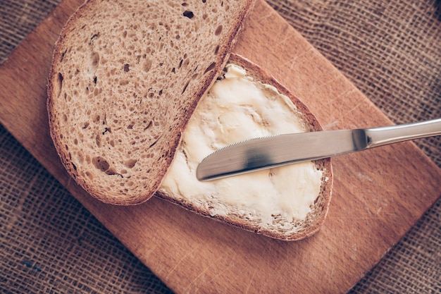 Close-up slice of bread with butter and knife on the wooden desk