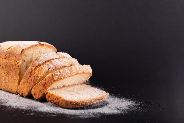 Close up sliced french lean bread with flour on a black background Concept recipe of handmade bread