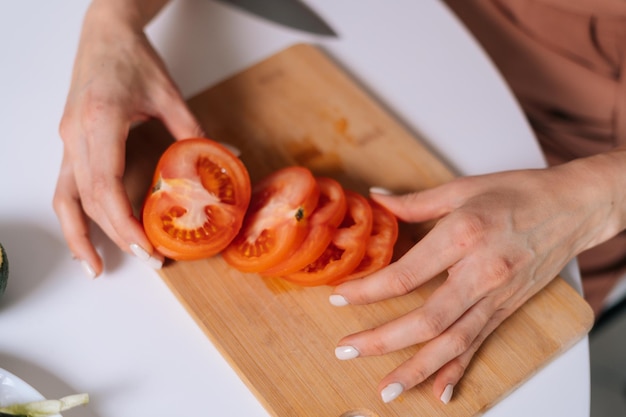 木の板、認識できない女性の手にスライスされた赤いフレッシュトマトのクローズアップ。健康的な食事の概念。