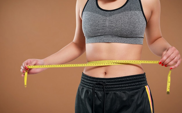 Close up of slim woman measuring her waist's size with tape measure. Isolated on yellow background.