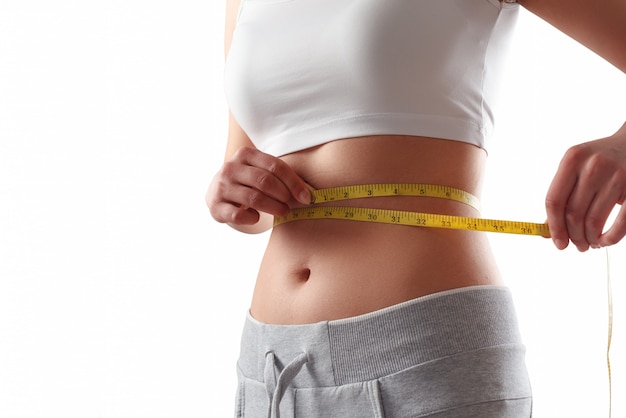 Photo close up of slim woman measuring her waist's size with tape measure.