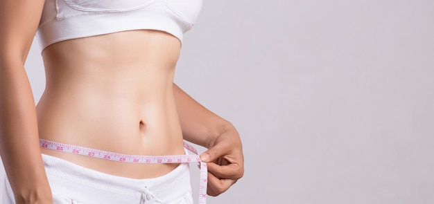 Close up slim young woman measuring her thin waist with a tape measure