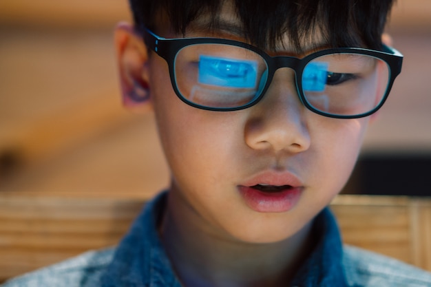 Foto close-up, slimme blik aziatische preteen / tiener staren naar computer laptop scherm met concentratie en opwinding over gamification, het dragen van blauw licht blokkerende bril. reflectie van computerscherm.