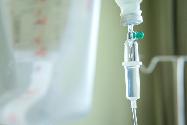 Close up of a slow intravenous drip with a blurred lit neon in the background in a hospital room