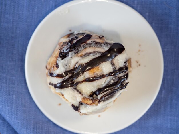 Primo piano di un piccolo panino alla cannella versato con cioccolato in un piatto bianco. tovagliolo di lino blu. messa a fuoco selettiva, delizioso dessert dolce, vista dall'alto, disposizione piatta