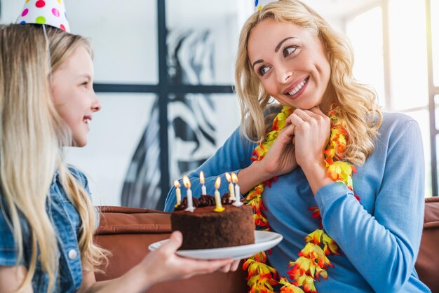 Close up of small girl kid presenting birthday cake to her mom
at home