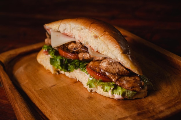 Close-up of a small sandwich of grilled chicken, tomato and lettuce on a wooden board.