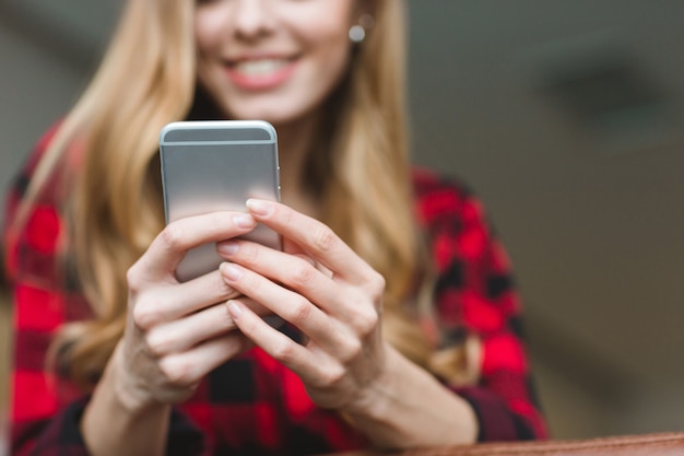 Close up of smaptphone used by beautiful smiling young woman in checkered shirt