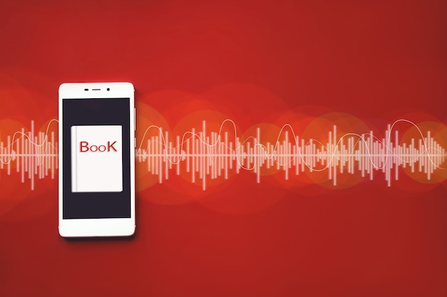 オーディオトラックと赤い背景のスマートフォンとオーディオブックのクローズアップ。オーディオ、聞いてください。オーディオブックのコンセプト。