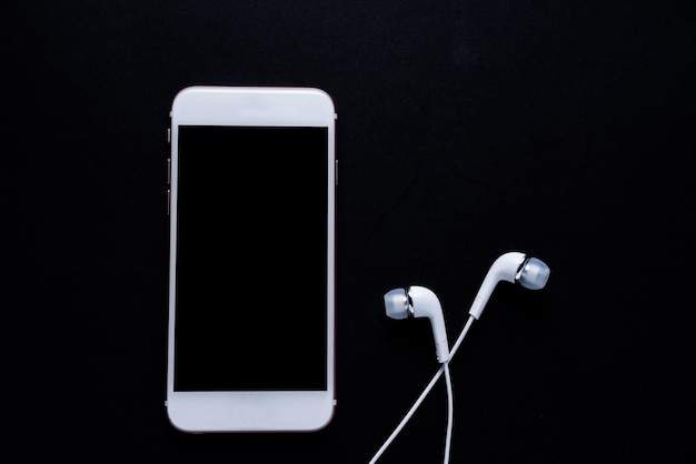 Photo close-up of smart phone and in-ear headphones against black background