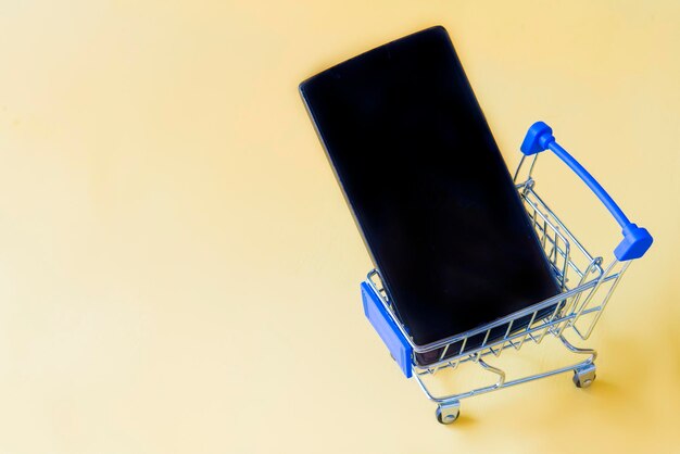 Close-up of smart phone in shopping cart against yellow background