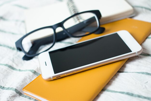 Photo close-up of smart phone with eyeglasses on bed