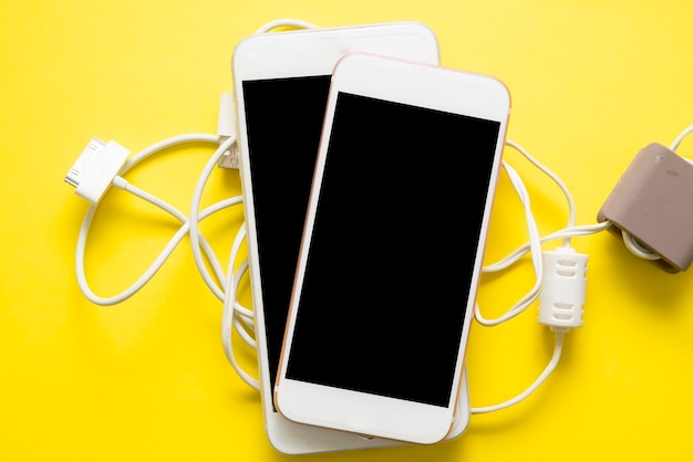 Close-up of smart phones with usb cables on yellow background