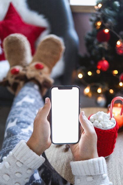 Close-up smartphone met leeg scherm mockup op vakantie achtergrond met kerstboom, klant telefoon in de hand houden, online winkelen, cadeaus kopen, informatie zoeken, browsen apps