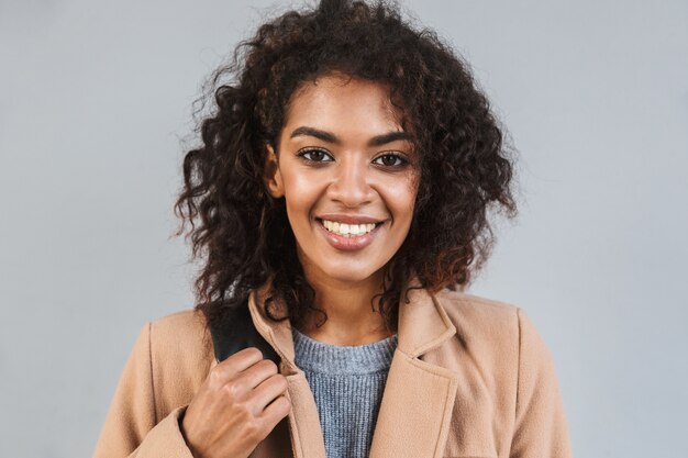 Close up of a smiling african woman wearing coat, carrying jacket isolated over gray