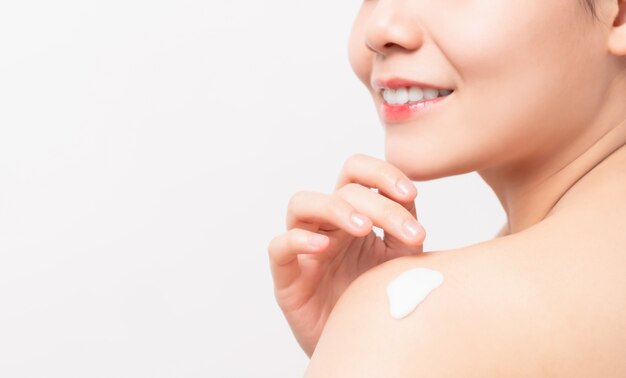 Close up of smiling Asian woman hand holding and applying moisturiser on shoulder, Body lotion, isolated on white wall