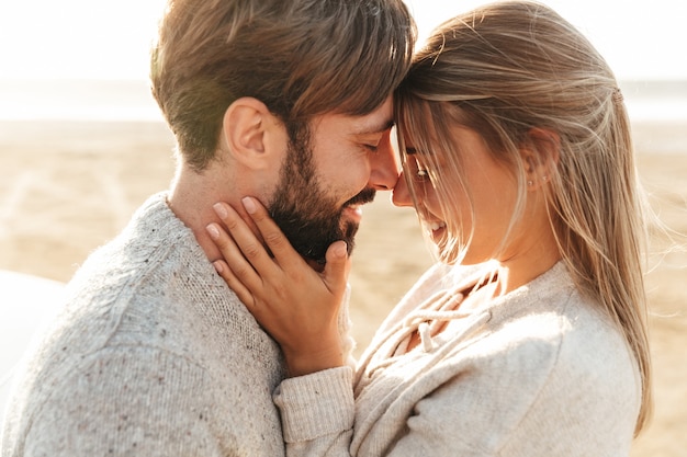 Close up of a smiling beautiful young couple embracing while standing at the beach