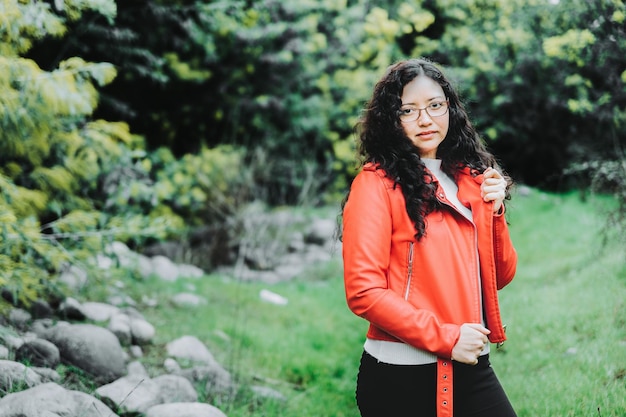 Close up of a smiling curly brunette woman, wearing a red leather jacket in a chilly scenery. Copy