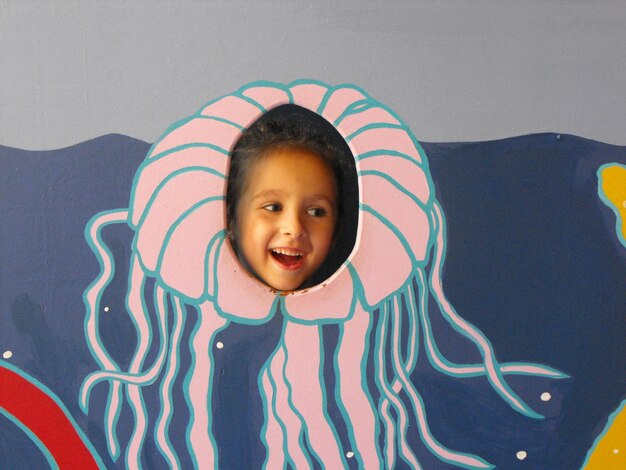 Photo close-up of smiling cute girl looking through hole with painted jelly fish