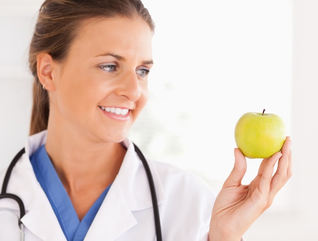 Close up of a smiling doctor with stethoscope looking at an appl