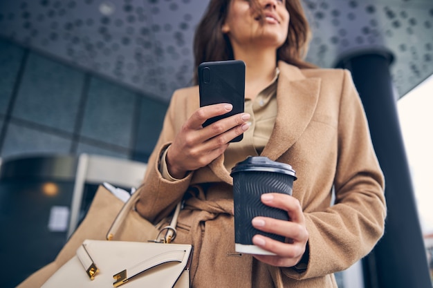 Close up on a smiling female holding a disposable coffee paper cup in her hands