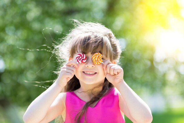 Foto close-up di una ragazza sorridente che tiene dei lecca-lecca nel parco