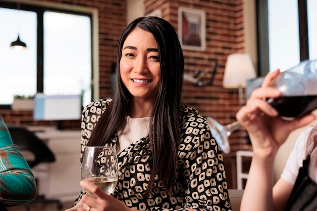 Close up of a smiling, happy, glad young adult asian woman, girl enjoying social life, drinking wine glass at friends, mates, partners apartment, home, house made party, reunion, gathering.