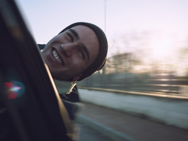 Foto close-up di un uomo sorridente in macchina contro il cielo