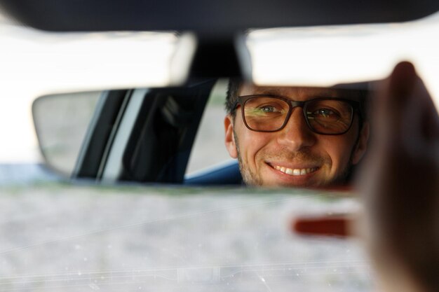 Photo close-up of smiling man looking in rear-view mirror