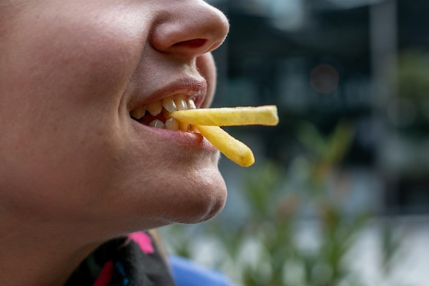 Foto close-up di una persona sorridente che mangia una patatina fritta che rappresenta i concetti di snack fast food