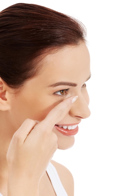 Close-up of smiling woman applying contact lens against white background