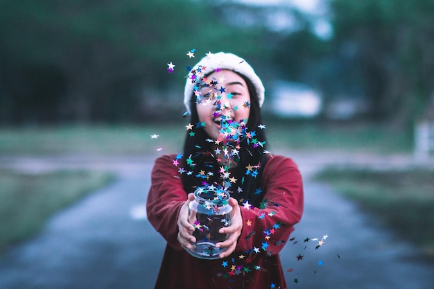 close-up of smiling woman throwing confetti against trees