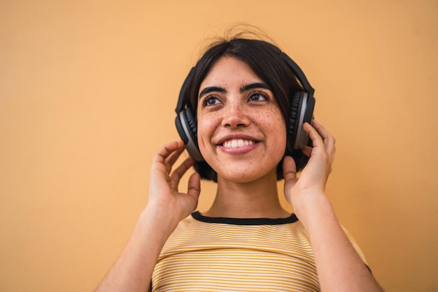 ベージュ色の背景にヘッドホンをかぶった笑顔の女性のクローズアップ