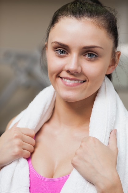 Chiuda su di una donna sorridente con l'asciugamano intorno al collo in palestra