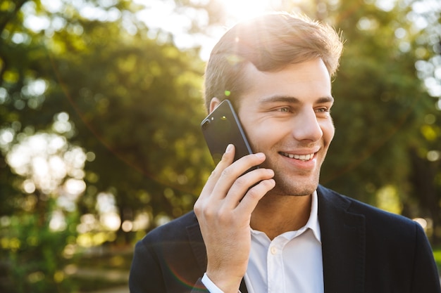 Close up of a smiling young businessman walking outdoors, talking on mobile phone