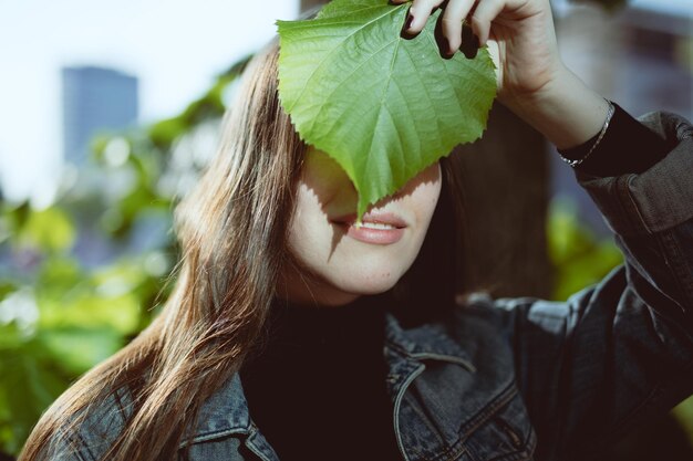 Photo close-up of smiling young woman covering face with leaf