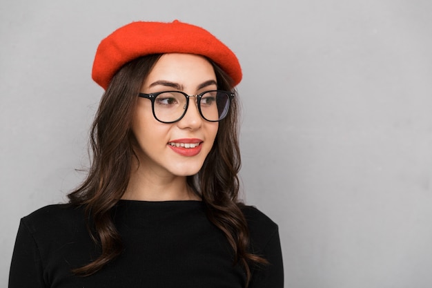 Close up of a smiling young woman in eyeglasses over gray background, looking away