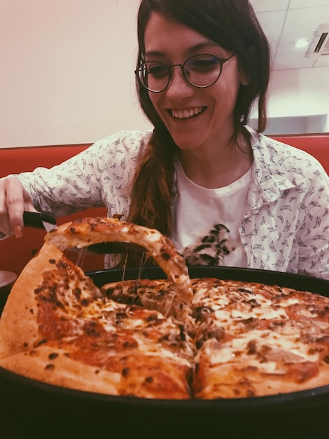 Foto close-up di una giovane donna sorridente che mangia una pizza