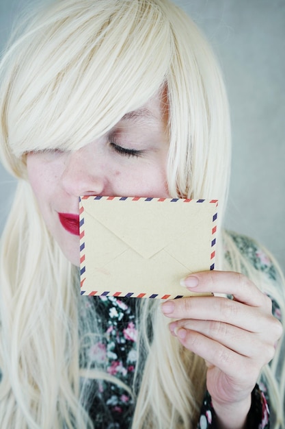 Photo close-up of smiling young woman smelling envelope