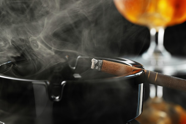 Photo close up of smoking cigar and whiskey glass on table